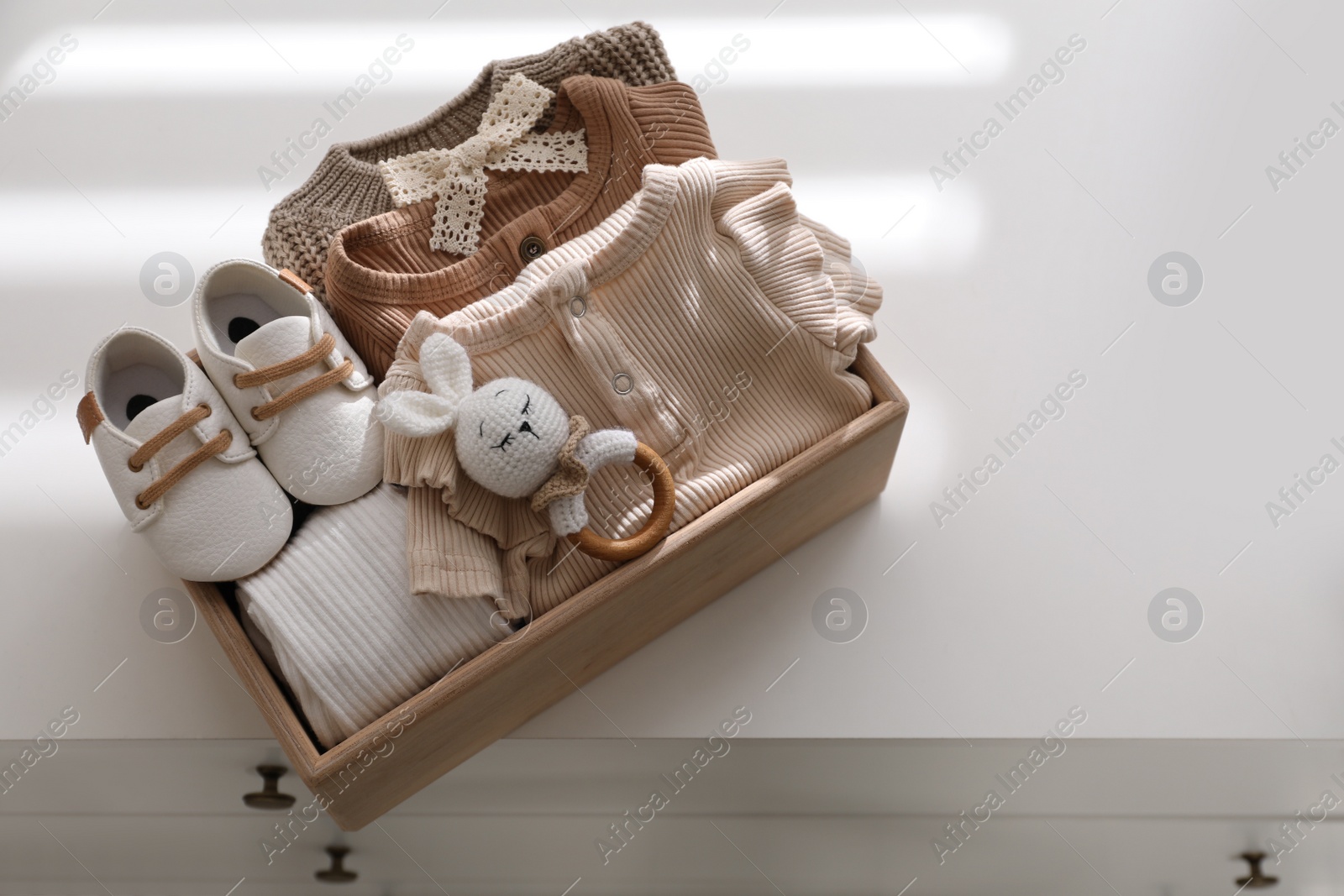 Photo of Wooden crate with children's clothes, shoes and toy on chest of drawers