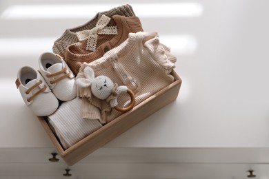 Photo of Wooden crate with children's clothes, shoes and toy on chest of drawers
