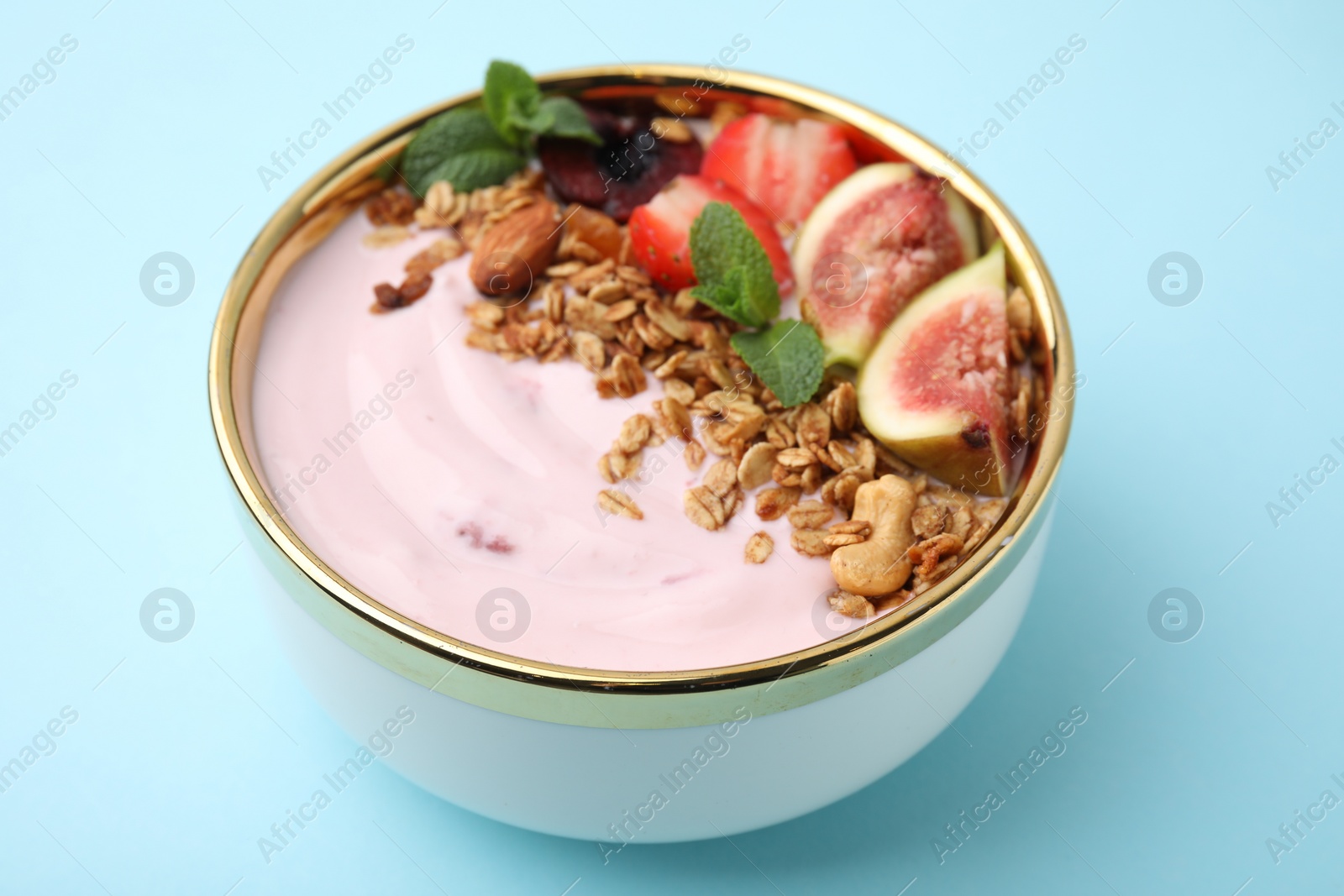 Photo of Bowl with yogurt, fruits and granola on light blue background, closeup