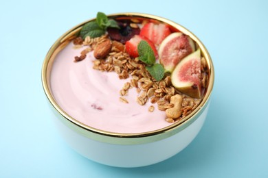 Bowl with yogurt, fruits and granola on light blue background, closeup