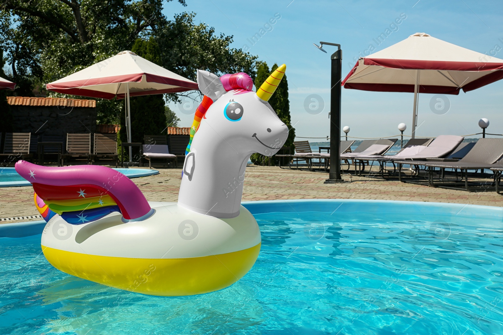 Photo of Funny inflatable unicorn ring floating in swimming pool on sunny day, outdoors. Space for text