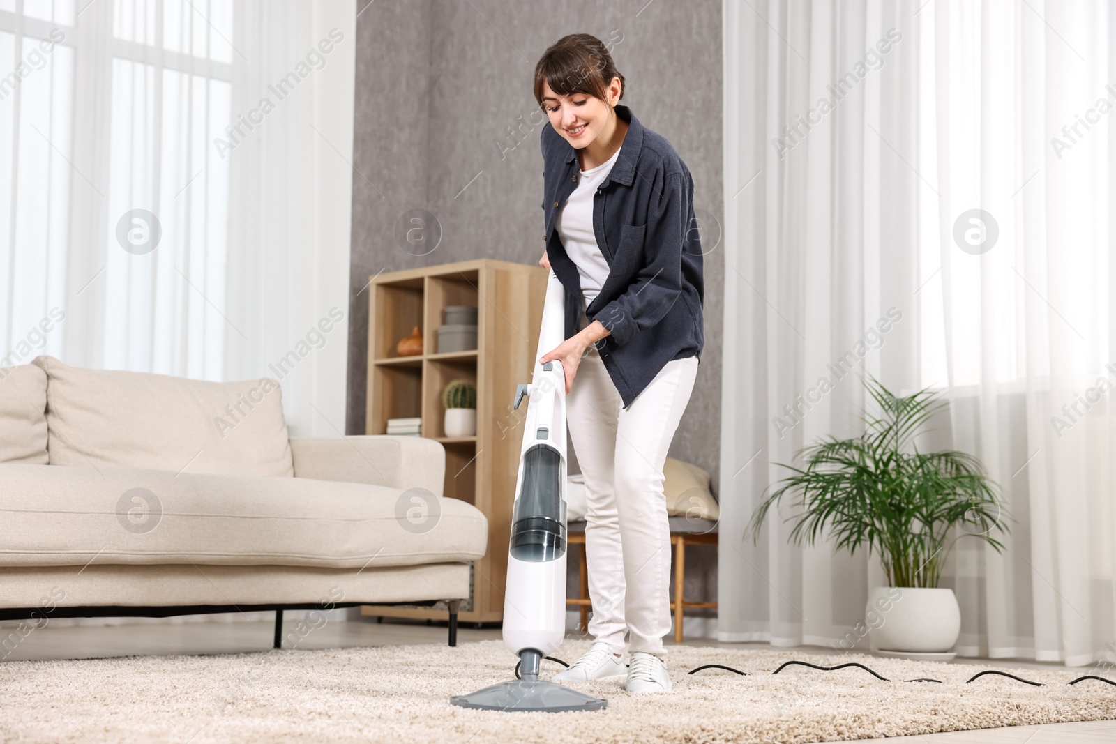 Photo of Happy young housewife vacuuming carpet at home