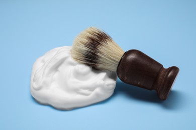 Photo of Brush with shaving foam on light blue background, closeup