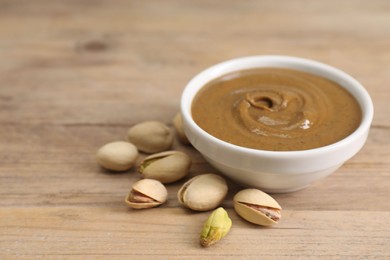 Delicious nut butter in bowl and pistachios on wooden table