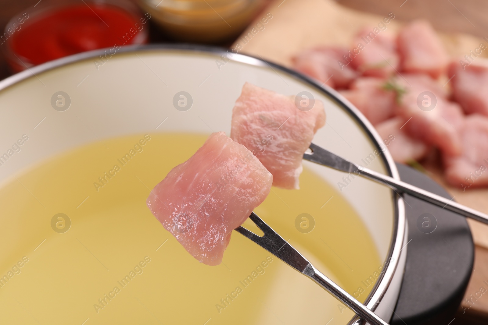 Photo of Forks with pieces of raw meat and fondue pot, closeup