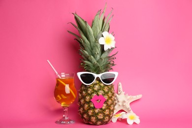 Funny pineapple with cocktail, plumeria flowers and starfish on pink background. Creative concept