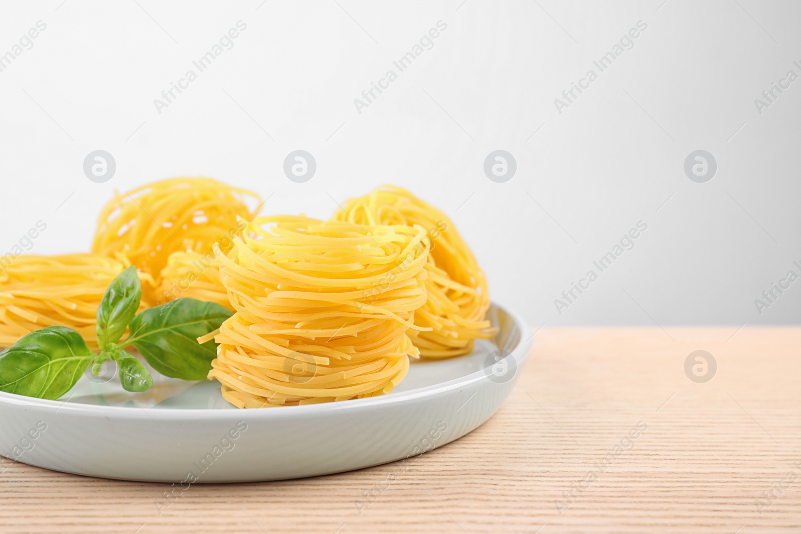 Photo of Uncooked tagliatelle pasta on wooden table against grey background