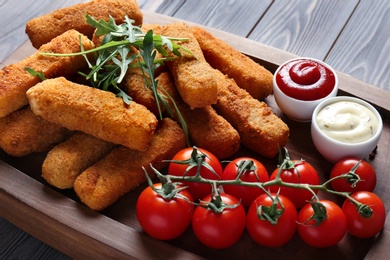 Photo of Board with cheese sticks, sauces and tomatoes on table, closeup