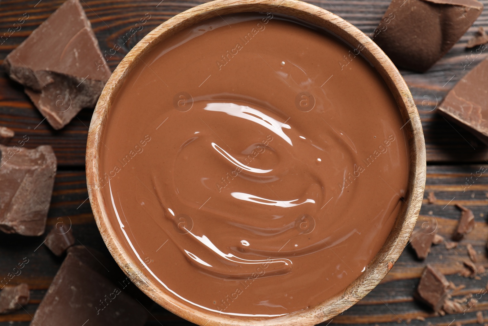 Photo of Tasty milk chocolate paste in bowl and pieces on wooden table, top view