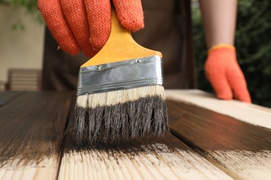 Photo of Man applying wood stain onto wooden surface against blurred background, closeup