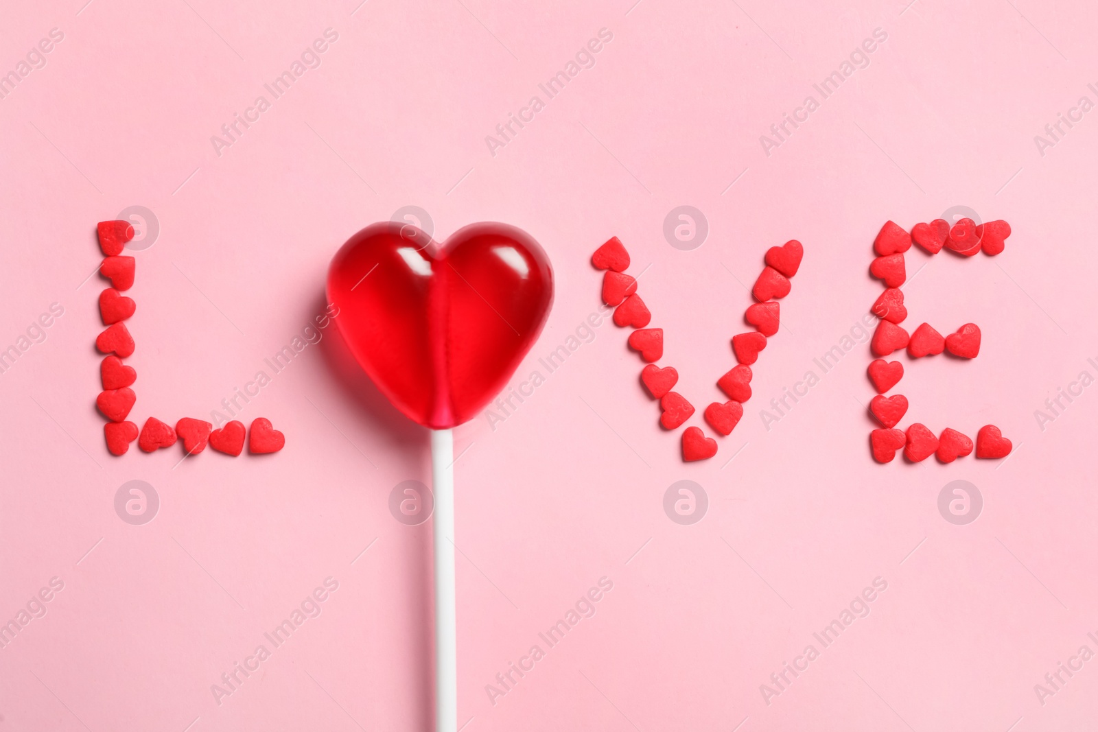 Photo of Word Love made with heart shaped lollipop and sprinkles on pink background, flat lay. Valentine's day celebration