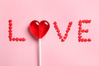 Photo of Word Love made with heart shaped lollipop and sprinkles on pink background, flat lay. Valentine's day celebration