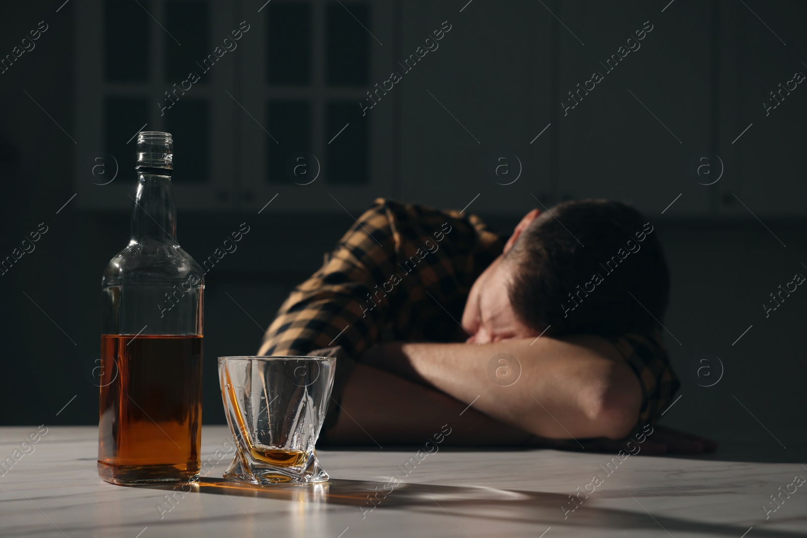 Photo of Addicted man sleeping at table in kitchen, focus on alcoholic drink. Space for text