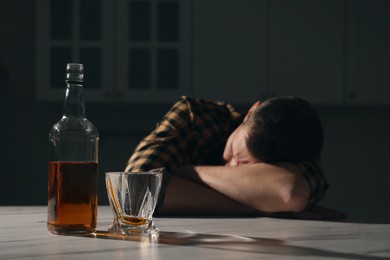 Photo of Addicted man sleeping at table in kitchen, focus on alcoholic drink. Space for text