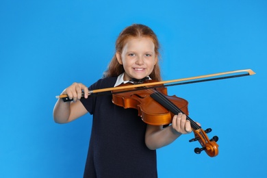 Preteen girl playing violin on light blue background