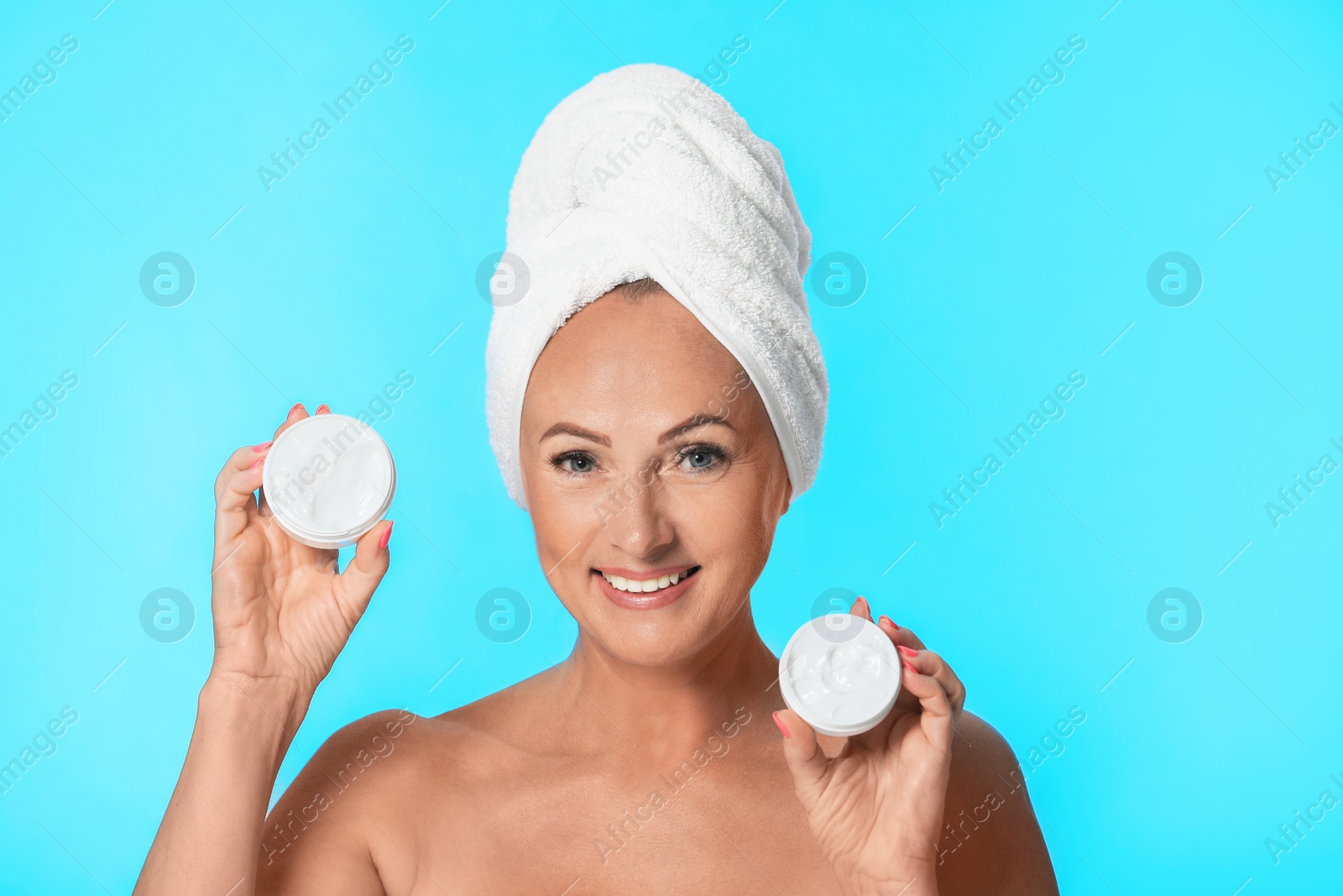 Photo of Portrait of beautiful mature woman with perfect skin holding jars of cream on light blue background