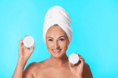 Photo of Portrait of beautiful mature woman with perfect skin holding jars of cream on light blue background