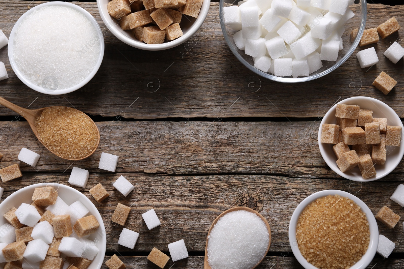 Photo of Frame of bowls and spoons with different types of sugar on wooden table, flat lay. Space for text