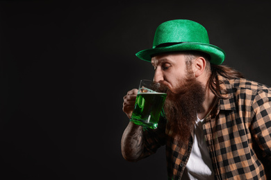 Bearded man drinking green beer on black background, space for text. St. Patrick's Day celebration