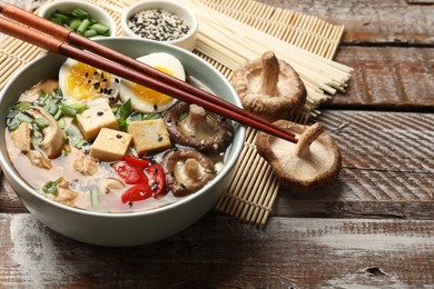 Noodle soup. Bowl of delicious ramen, ingredients and chopsticks on wooden table, closeup. Space for text