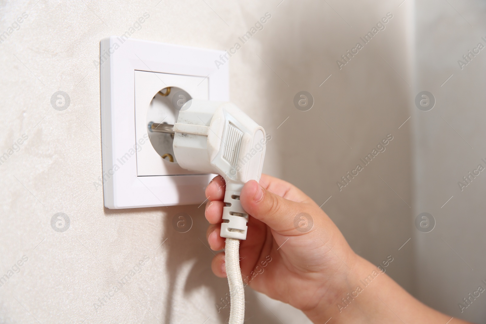 Photo of Little child playing with electrical socket and plug indoors, closeup. Dangerous situation