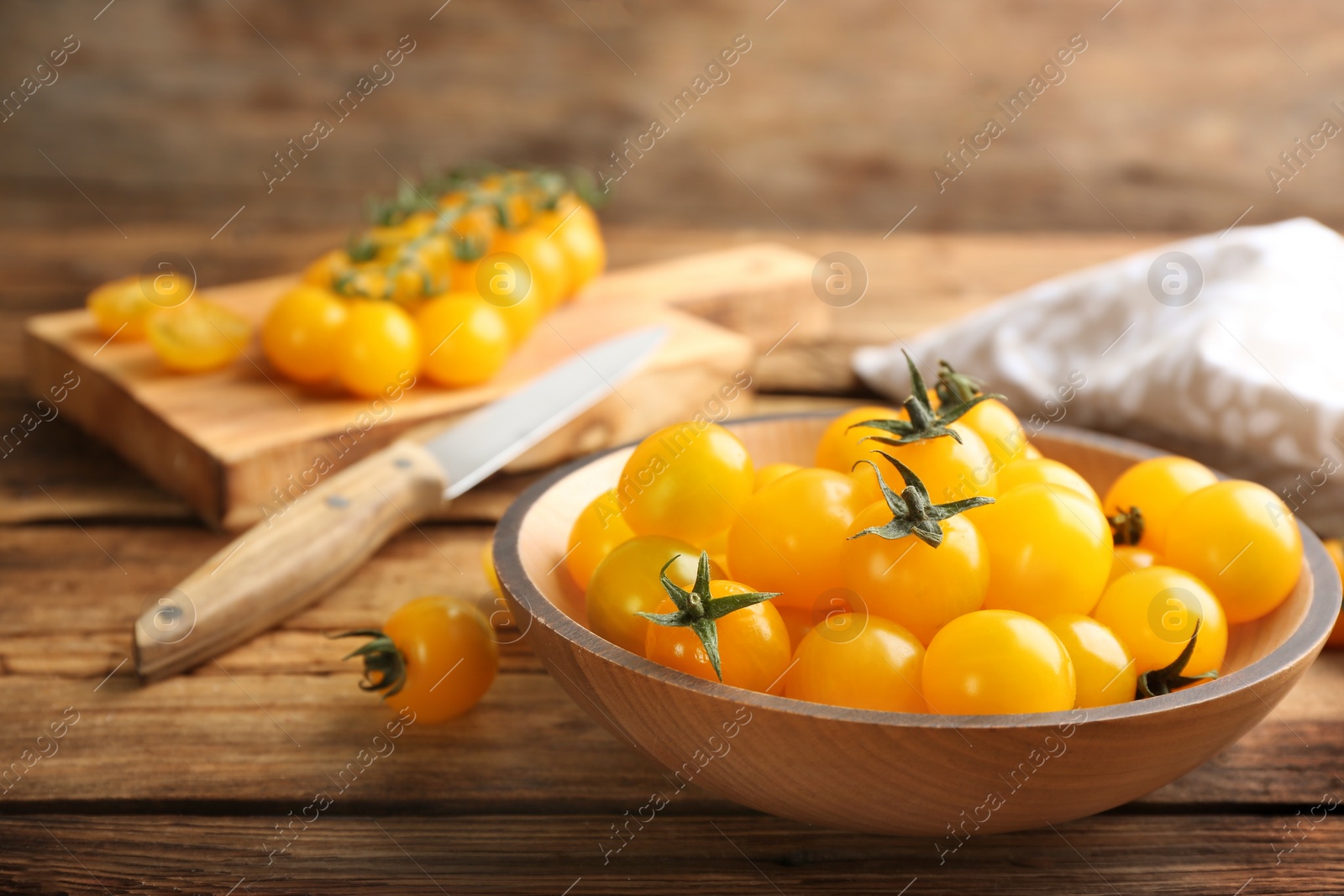 Photo of Ripe yellow tomatoes in bowl on wooden table