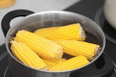 Photo of Stewpot with water and corn cobs on stove, closeup