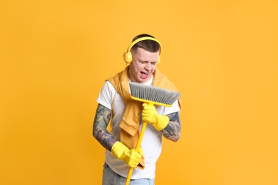 Photo of Handsome young man with floor brush singing on orange background