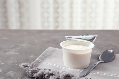 Photo of Plastic cup of fresh yogurt and napkin with spoon on table. Space for text