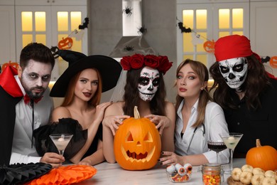 Photo of Group of people in scary costumes with cocktails and carved pumpkin celebrating Halloween indoors