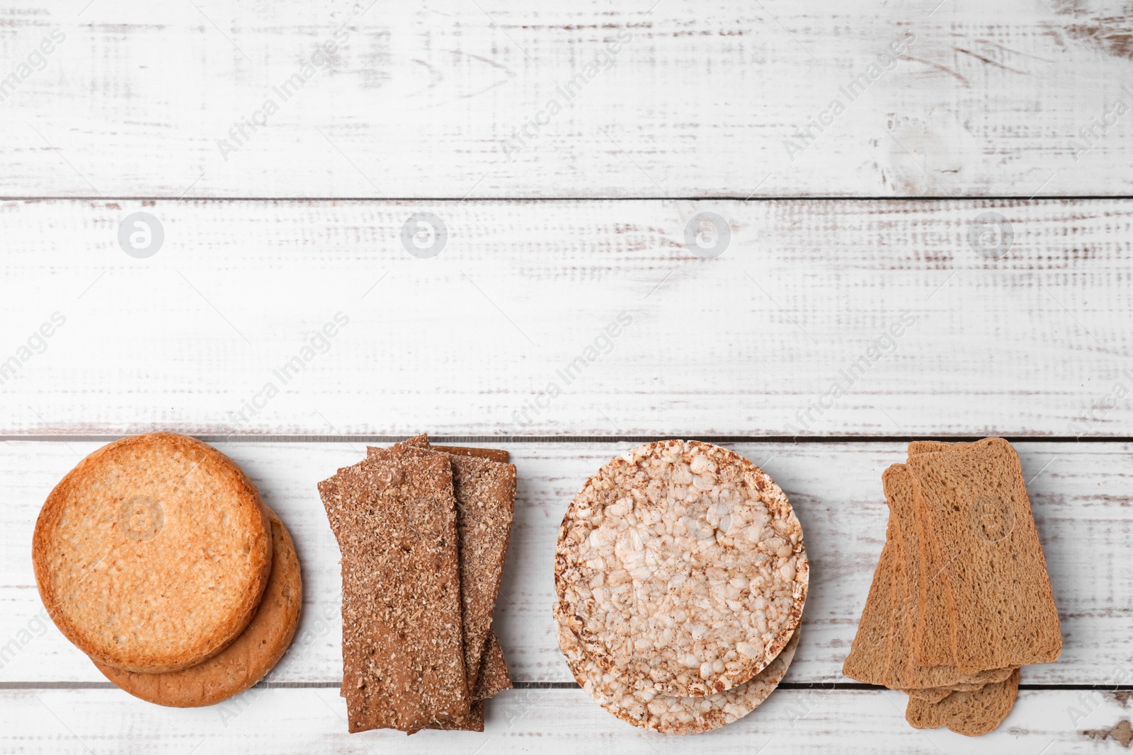 Photo of Rye crispbreads, rice cakes and rusks on white wooden table, flat lay. Space for text