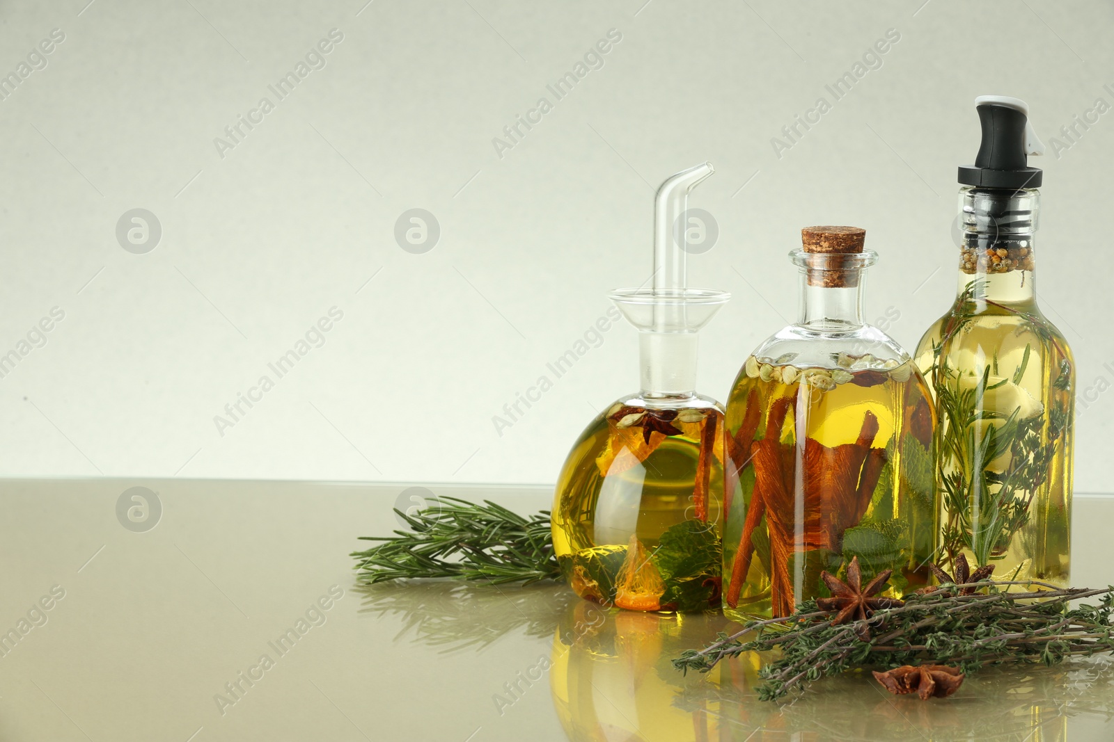 Photo of Cooking oil with different spices and herbs in bottles on beige table. Space for text