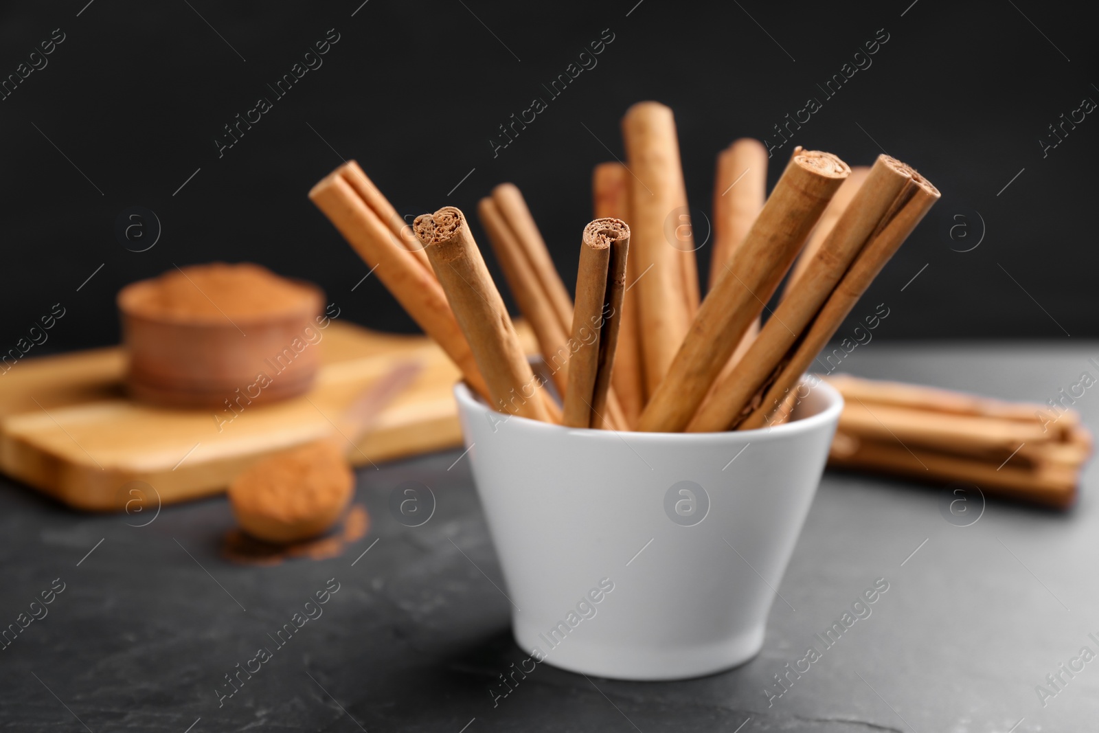 Photo of Aromatic cinnamon sticks in bowl on black table