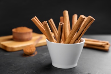 Photo of Aromatic cinnamon sticks in bowl on black table