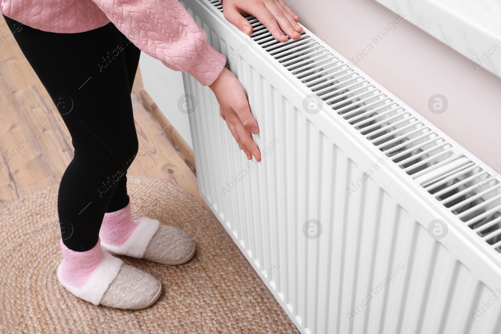 Photo of Girl warming hands on heating radiator indoors, closeup