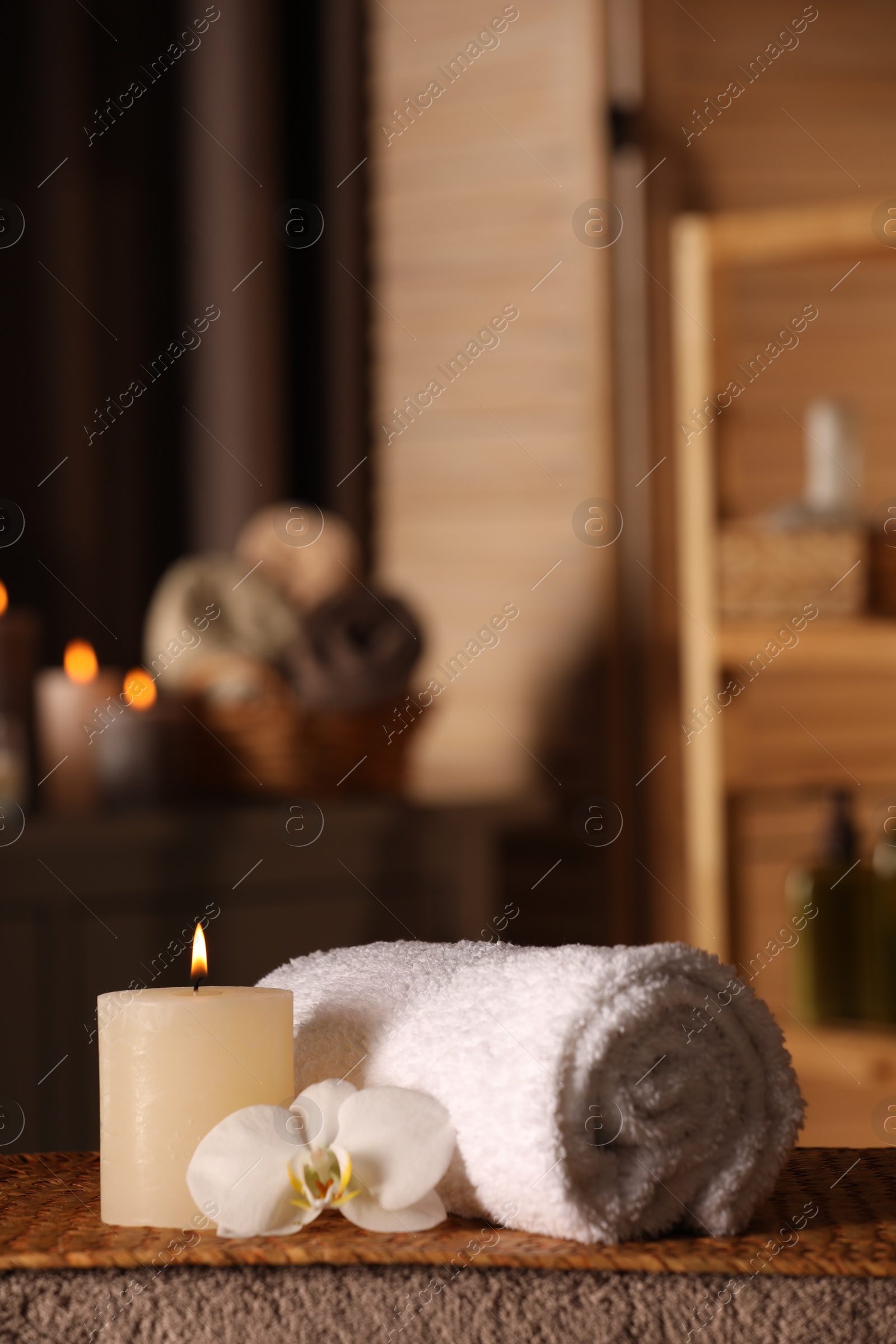 Photo of Spa composition with candle, orchid flower and rolled towel on massage table in wellness center, space for text