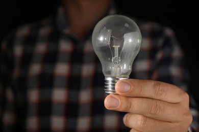 Man holding incandescent light bulb on dark background, closeup. Space for text