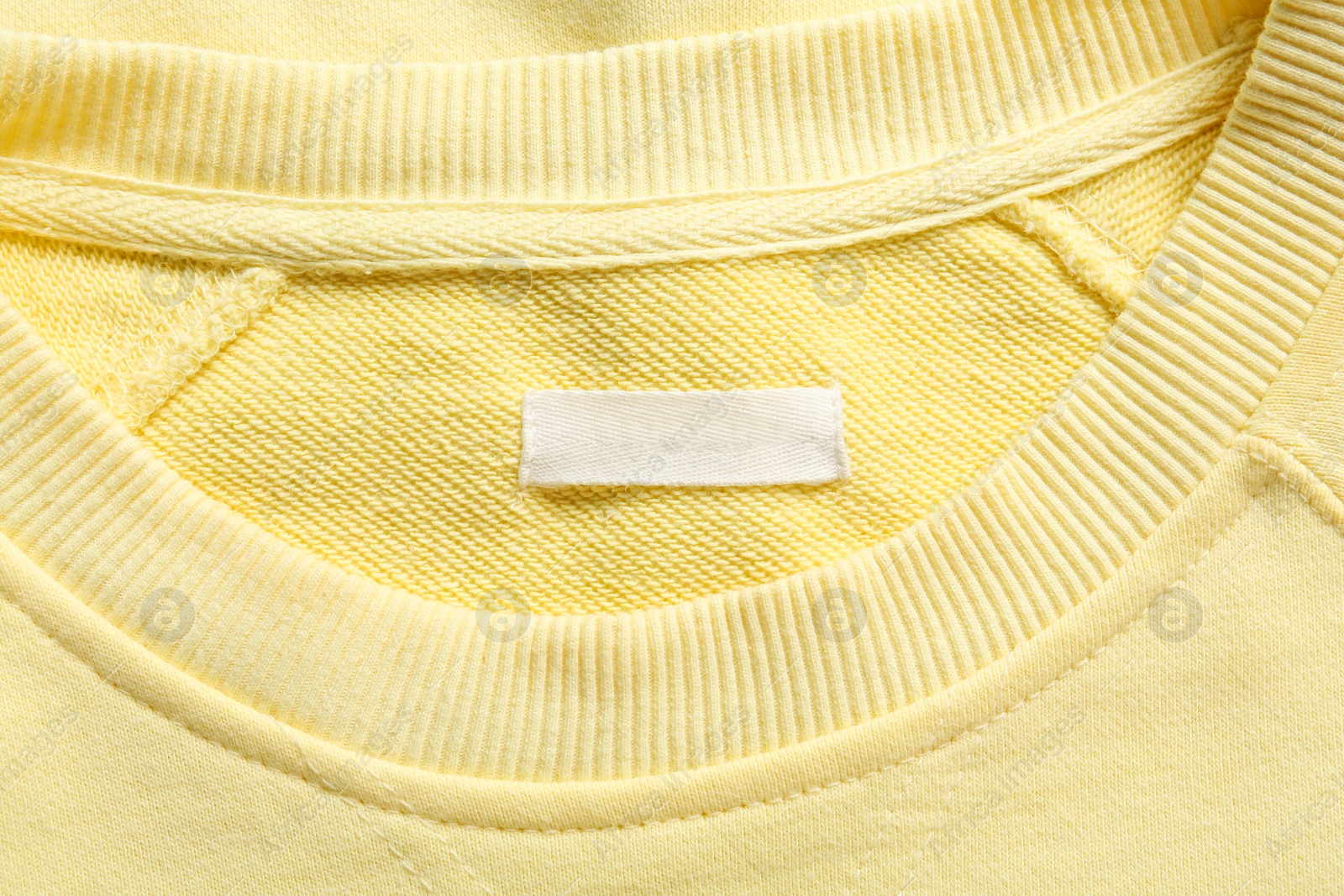 Photo of Blank clothing label on yellow sweater, top view