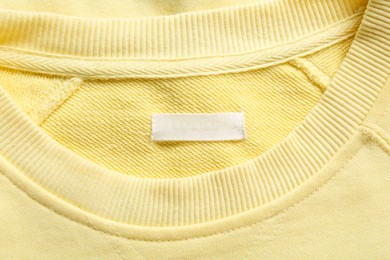 Photo of Blank clothing label on yellow sweater, top view