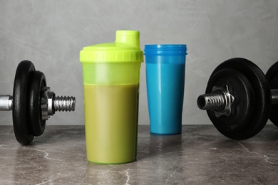 Photo of Bottles with protein shakes and dumbbells on grey table