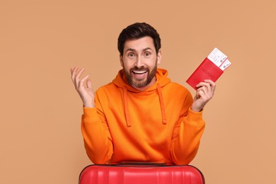 Happy man with passport, suitcase and tickets on beige background