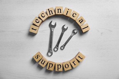 Photo of Flat lay composition with words TECHNICAL SUPPORT and wrenches on wooden background