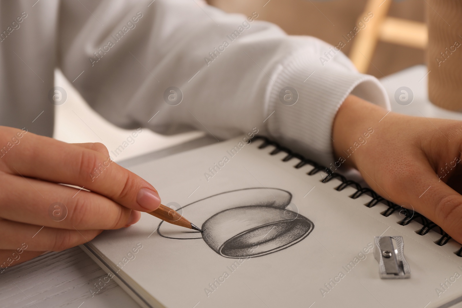 Photo of Woman drawing cup of drink with graphite pencil in sketchbook at table, closeup