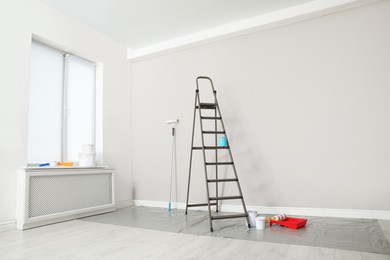 Photo of Decorator's tools and ladder near white wall indoors