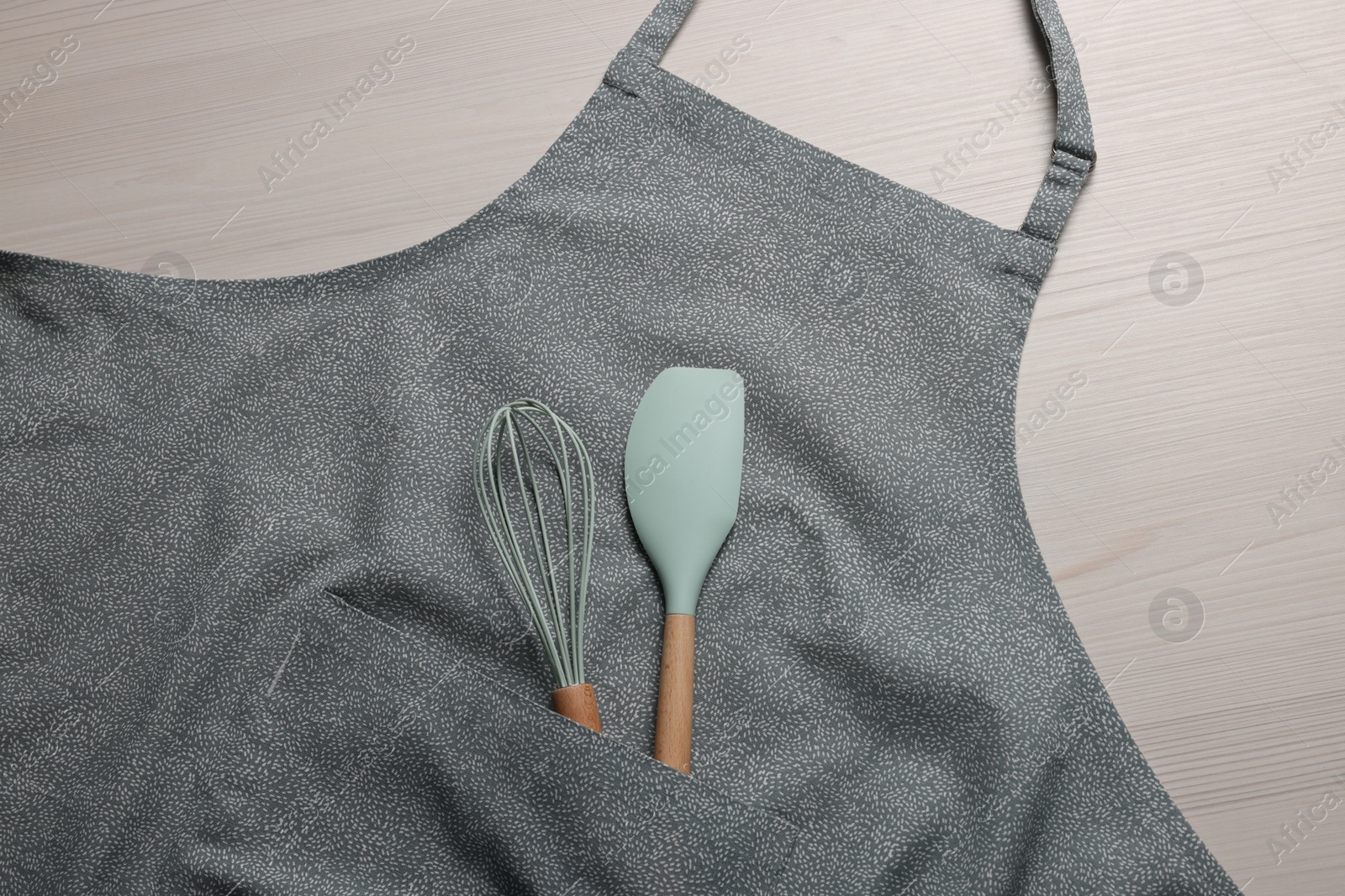 Photo of Stylish apron, spatula and whisk on white wooden table, top view