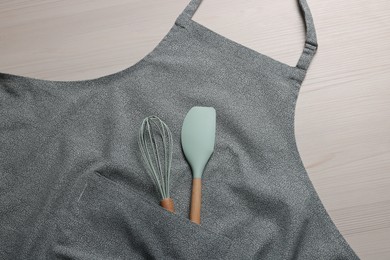 Stylish apron, spatula and whisk on white wooden table, top view