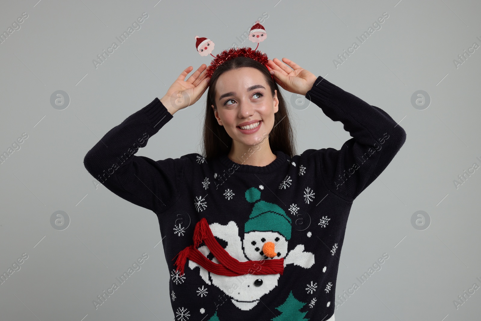 Photo of Happy young woman in Christmas sweater and Santa headband on grey background