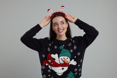 Happy young woman in Christmas sweater and Santa headband on grey background