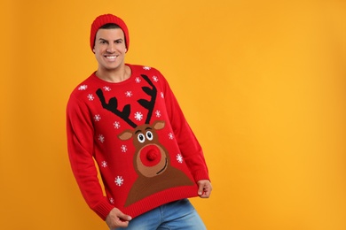 Photo of Happy man in hat showing his Christmas sweater on yellow background