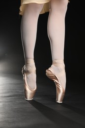 Ballerina in pointe shoes dancing on black background, closeup